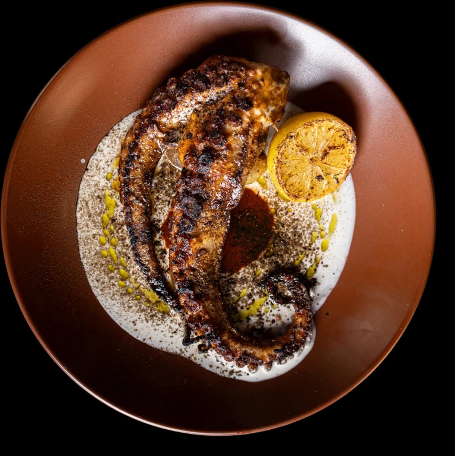 Grilled octopus on a terracotta plate over a white sauce, with half a grilled lemon