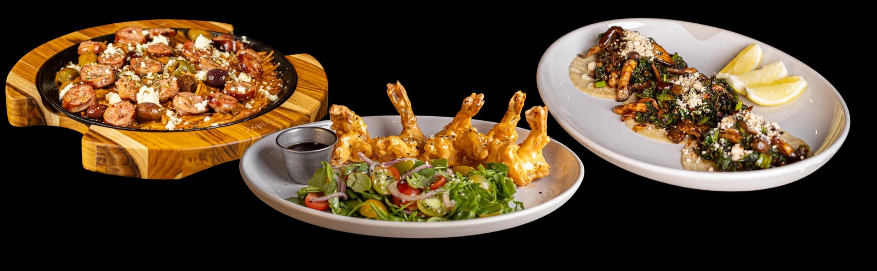 Three plates: noodles with sliced sausage on a wooden board, crispy shrimp with a salad, and three mushroom tacos