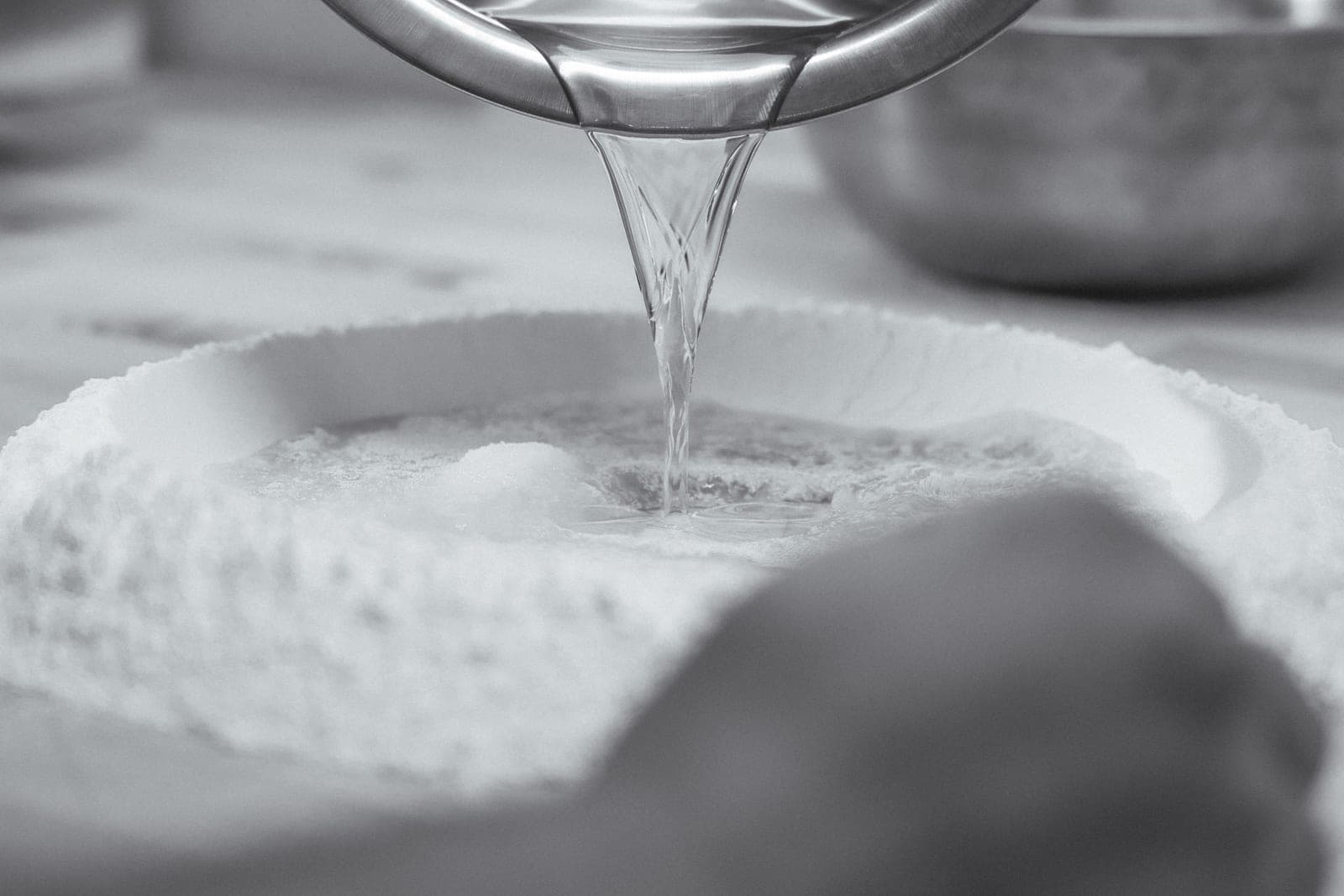 Water poured into a well of flour, in black and white
