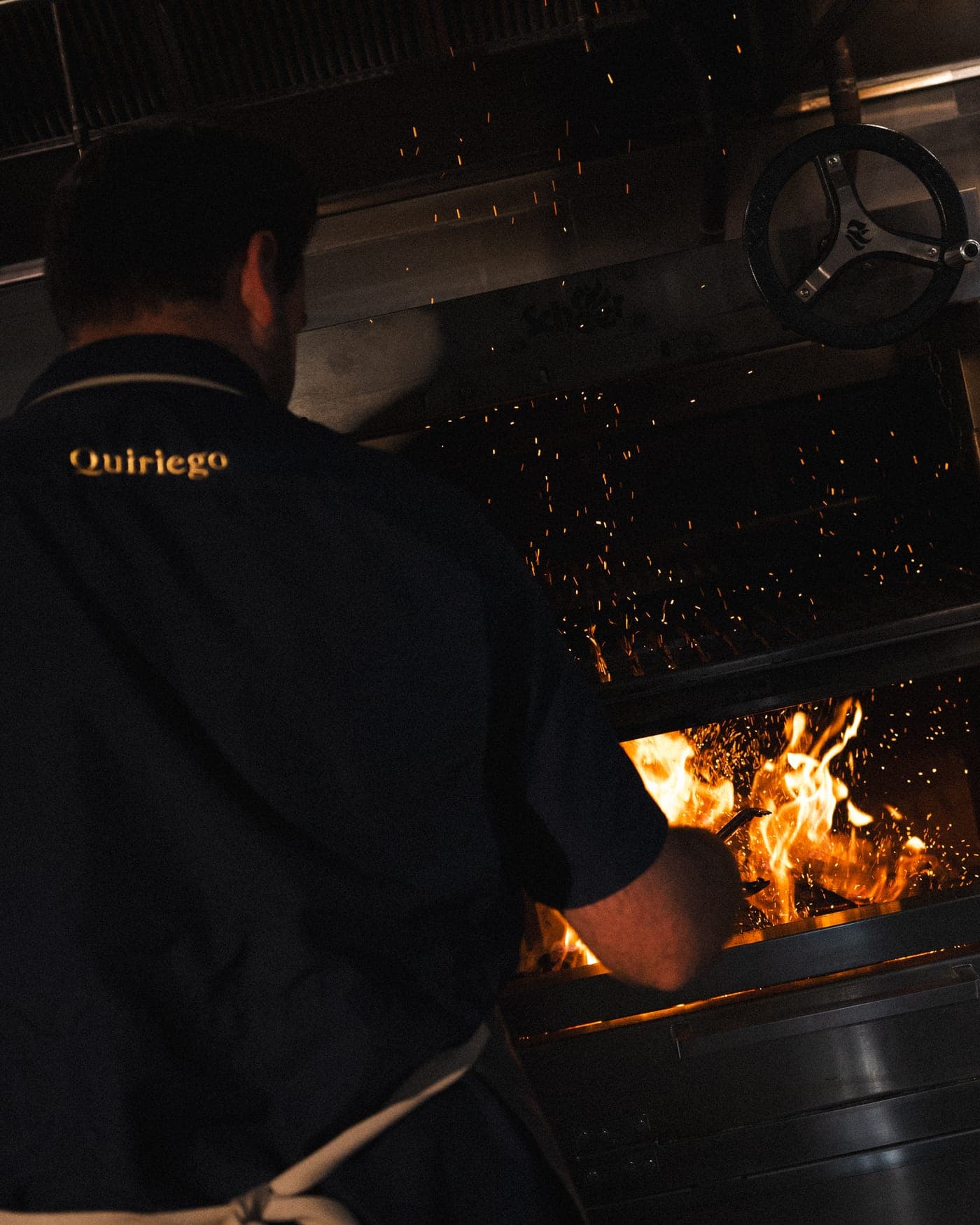 Un cocinero atiende el fuego de leña entre chispas